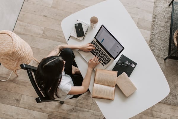 Person working on laptop at a café table with books and phone nearby