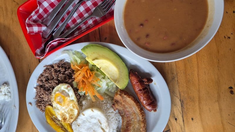 Bandeja paisa tradicional colombiana con frijoles, chicharrón, arroz, arepa y aguacate