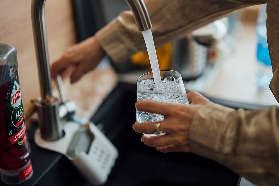 Person filling a glass of water at a kitchen tap