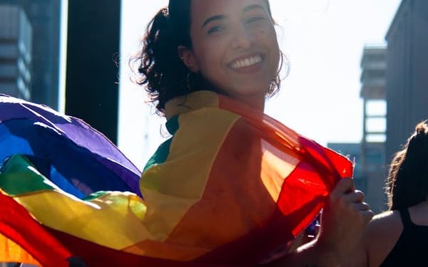 Woman smiling and holding a rainbow pride flag at a pride parade